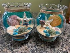 two glass vases with seashells and starfish in them on a counter