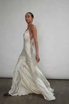 a woman in a long white dress is posing for the camera with her hand on her hip