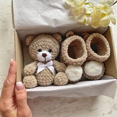 a hand holding a box with two crocheted teddy bears in it next to a flower