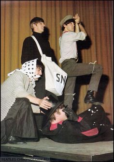 three young men sitting on top of each other in front of a curtain with one man holding a shopping bag