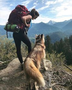 a woman with a backpack and her dog on top of a mountain looking at the view