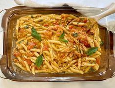 a casserole dish with pasta, tomatoes and basil on top is ready to be eaten