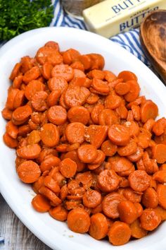 a white bowl filled with carrots on top of a table next to butter and parsley