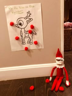 an elf is sitting on the floor in front of a sign that says, put his nose on the reindeer