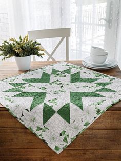 a green and white quilt sitting on top of a wooden table next to a potted plant