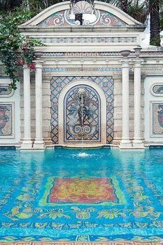 an outdoor pool with blue and yellow tiles on the floor next to a building that has a clock in it