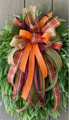 a wreath with orange, green and red ribbons hanging on a door front porch ornament