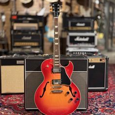 a red guitar sitting on top of a carpet next to amps and guitars in a room