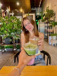 a woman sitting at a table with a green smoothie in her hand