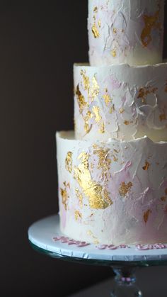 a three tiered cake with gold leaf designs on it's sides and white frosting