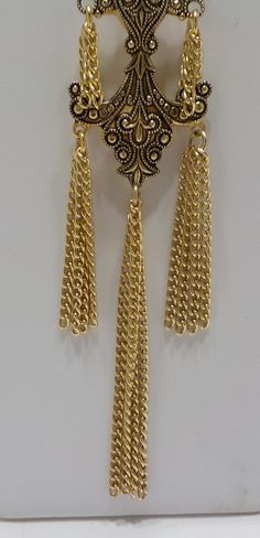 "Vintage gold tone dangling necklace resembling Damascene or Toledoware. 30\" gold tone pullover chain attached to a pendant measuring 1 1/4\" x 3 1/2\" including tassels. Gorgeous and in excellent condition." Metal Dangle Chain Necklace Costume Jewelry, Gold Brass Jewelry With Dangling Charms, Gold Long Dangle Necklace With Chain, Metal Long Dangle Necklace With Chain, Gold Metal Dangle Necklaces, Dangle Chain Long Necklace As Gift, Gold Metal Necklace With Pendant, Metal Long Dangle Necklace As A Gift, Metal Dangle Long Necklace For Gift