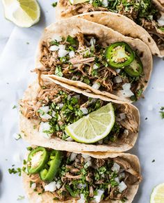 three shredded pork tacos with jalapenos, limes and cilantro