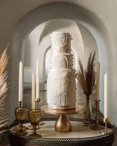 a white wedding cake sitting on top of a table next to candles and some feathers