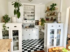 a kitchen with white cabinets and black and white checkered flooring, potted plants in the corner