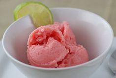 a white bowl filled with pink ice cream next to a lime slice