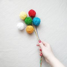 a person holding yarn balls in their hand and knitting them together to make a crochet ball bouquet