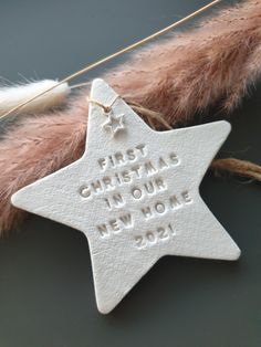 a white ceramic star ornament hanging from a string with the words first christmas, new home on it