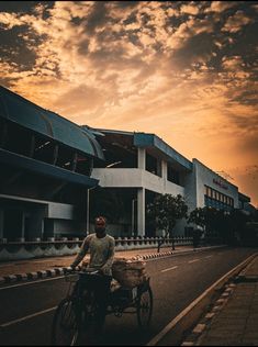 a man riding a bike down a street next to a tall building under a cloudy sky