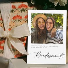 two women with hats and sunglasses are smiling next to a gift wrapped in white paper