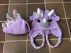 two crocheted hats with unicorn ears and tails, one is purple the other is pink