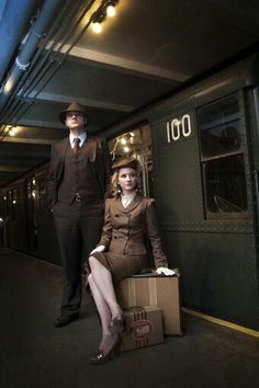 a man and woman dressed in business attire standing next to a train car with boxes on the floor