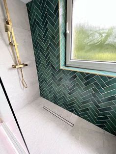 a bathroom with green and white tile on the walls, shower head, and window