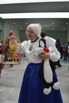 an older woman holding a stuffed animal in front of a birdcage and smiling at the camera