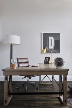 a desk with a clock, lamp and chair in a room that has hard wood floors