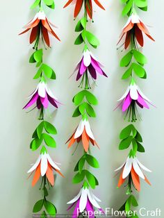 paper flowers are hanging on the wall with green and orange leaves attached to them,