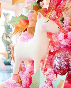 a pink and gold christmas tree with a white horse on it's head surrounded by ornaments