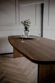 a wooden table with two wine glasses and a plate on it, in front of a white wall