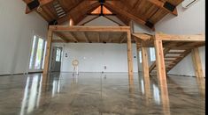 an empty room with wooden beams and ceiling fan in the center, surrounded by concrete flooring