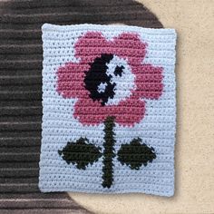 a crocheted square with a pink and black flower on the front, sitting on a beige surface