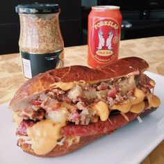 a sandwich with cheese and meat on it sitting on a plate next to a can of beer