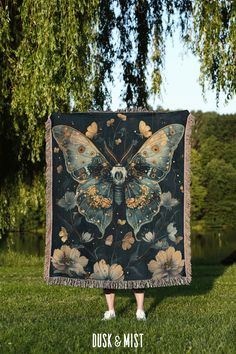 a woman standing in the grass holding up a blanket with a butterfly design on it