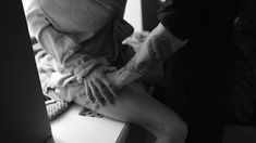 a woman with tattoos on her legs sitting on a counter next to a man in a suit