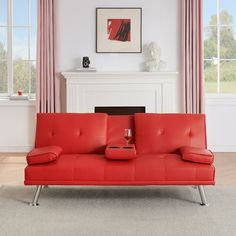 a red couch sitting in front of a window next to a fire place with a painting on the wall