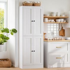 a kitchen with white cupboards and wooden flooring next to a potted plant