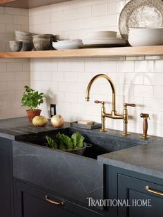 a kitchen sink with two faucets and some plates on the shelf above it