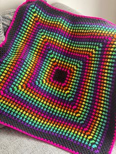 a crocheted square is sitting on top of a couch with a blanket around it