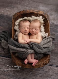 two twin babies cuddling in a wooden bowl