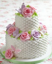 three tiered wedding cake with pink roses on top and green trim around the edges