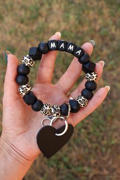 a hand holding a black and white bracelet with an i am heart charm on it