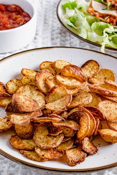 a white plate topped with potato wedges next to a bowl of salad