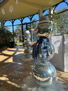 several shiny disco ball sculptures in front of a glass walled area with trees and bushes