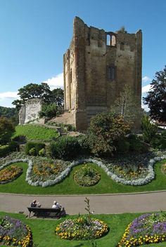 people sitting on a bench in the middle of a garden with flowers and plants around it