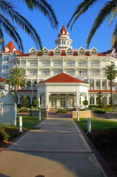 a large white building with red roof and palm trees in the foreground on a sunny day