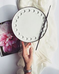 a person holding a white plate with dots on it next to a book and flower