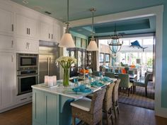 a kitchen with blue walls and white cabinetry has an island in the middle that is surrounded by chairs