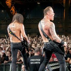 two shirtless men standing on stage in front of an audience with their backs to the camera